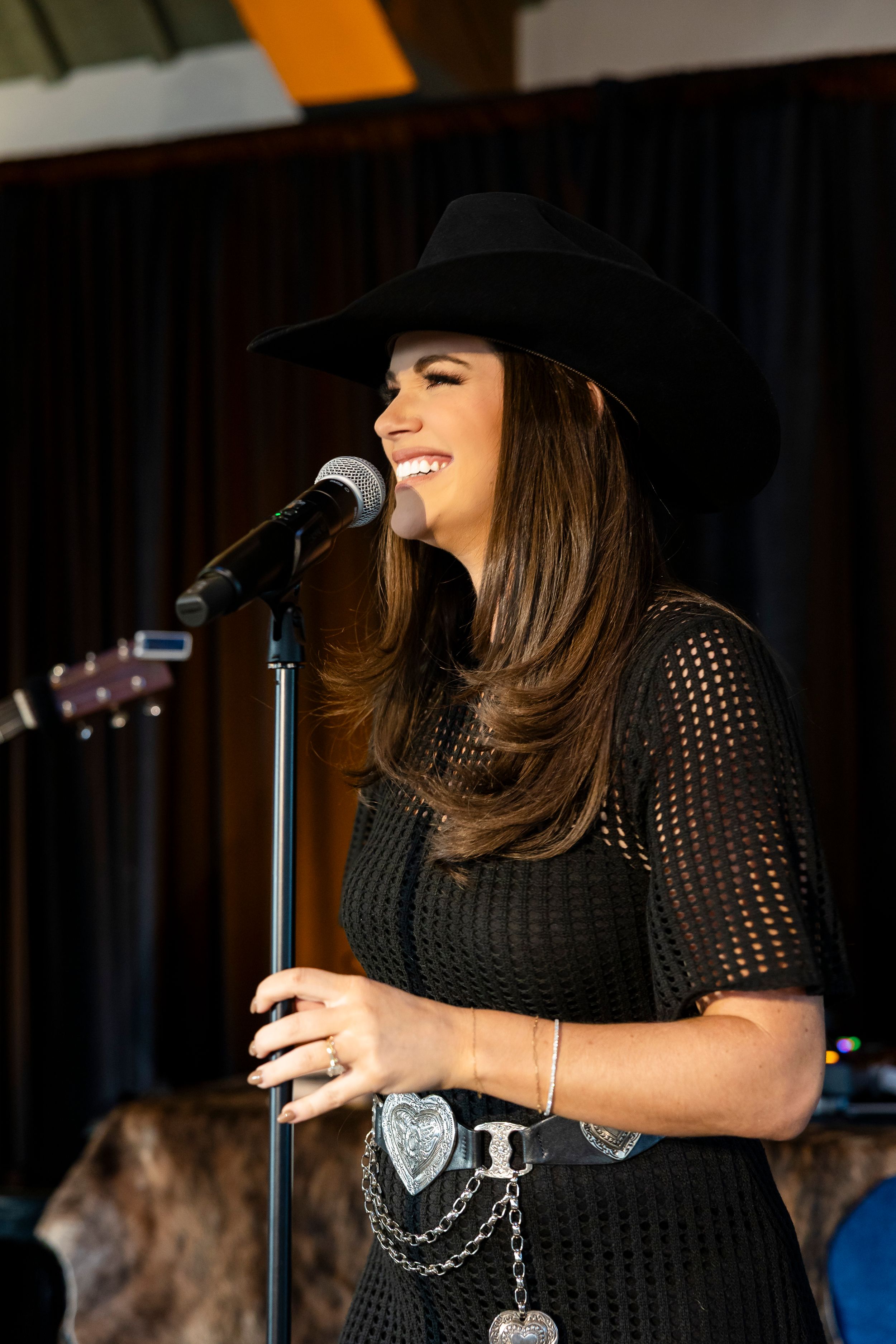 Performer singing on stage in a black mesh top and hat.