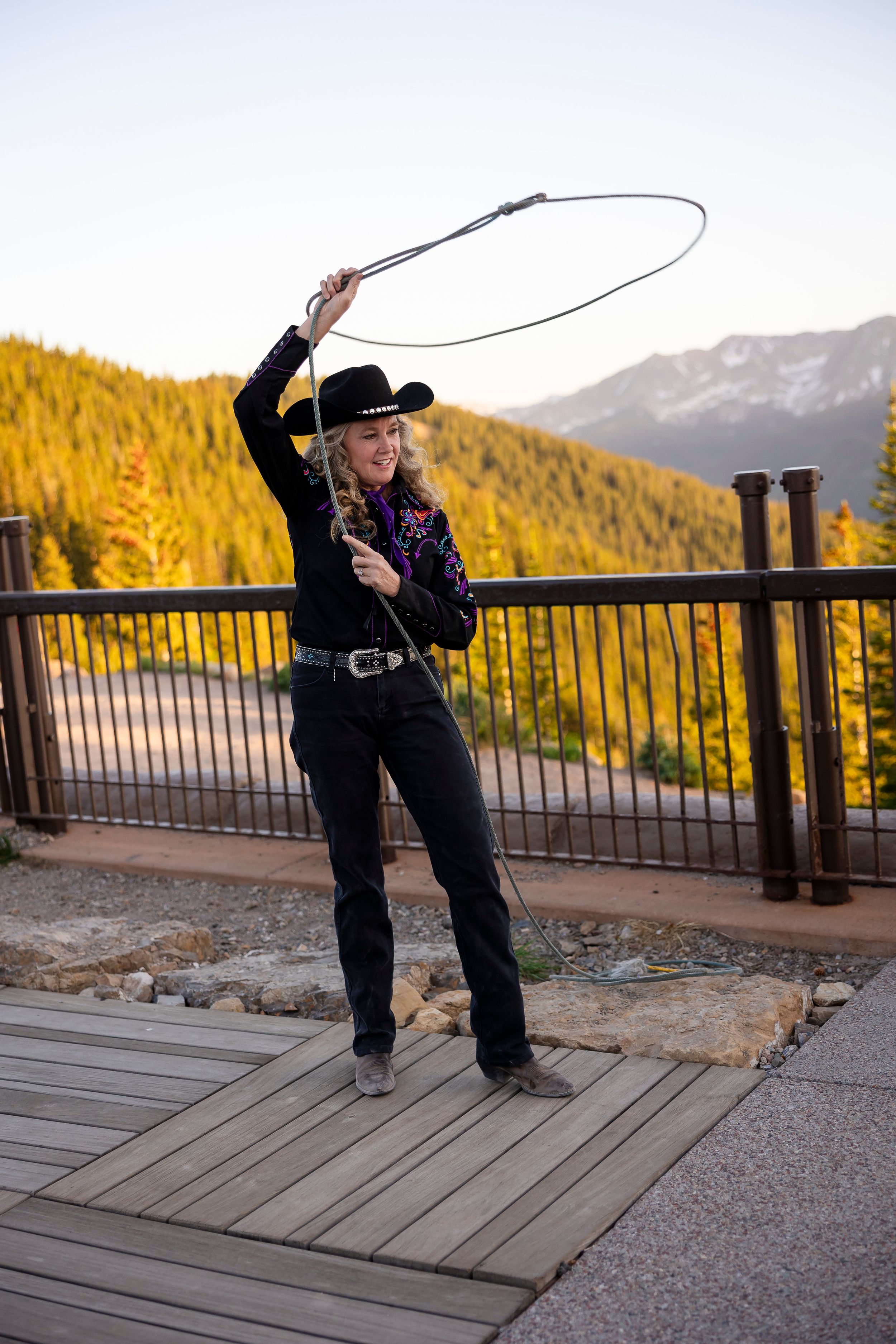 Person practicing lasso tricks on wooden deck with mountain backdrop.