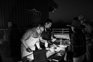Dark nighttime event with people gathered around tables at an outdoor venue.