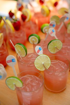 Row of pink tropical cocktails garnished with lime slices and straws.