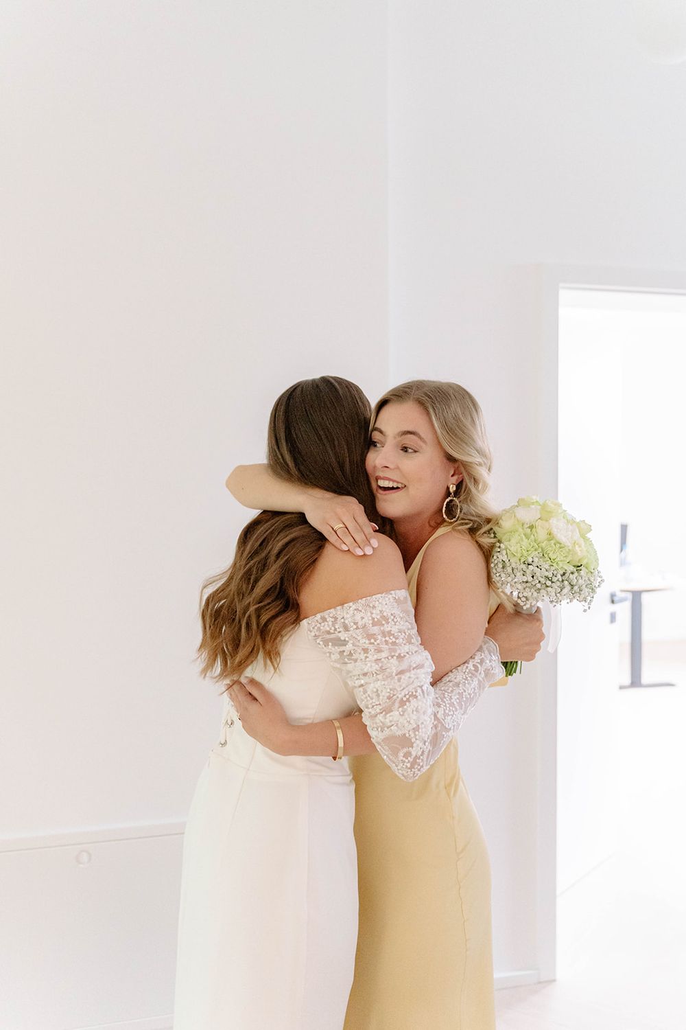 Two people share an emotional embrace while wearing formal attire in a bright indoor setting.