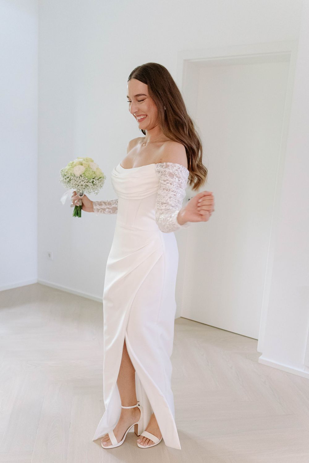 Woman in white off-shoulder dress posing gracefully in bright studio setting.