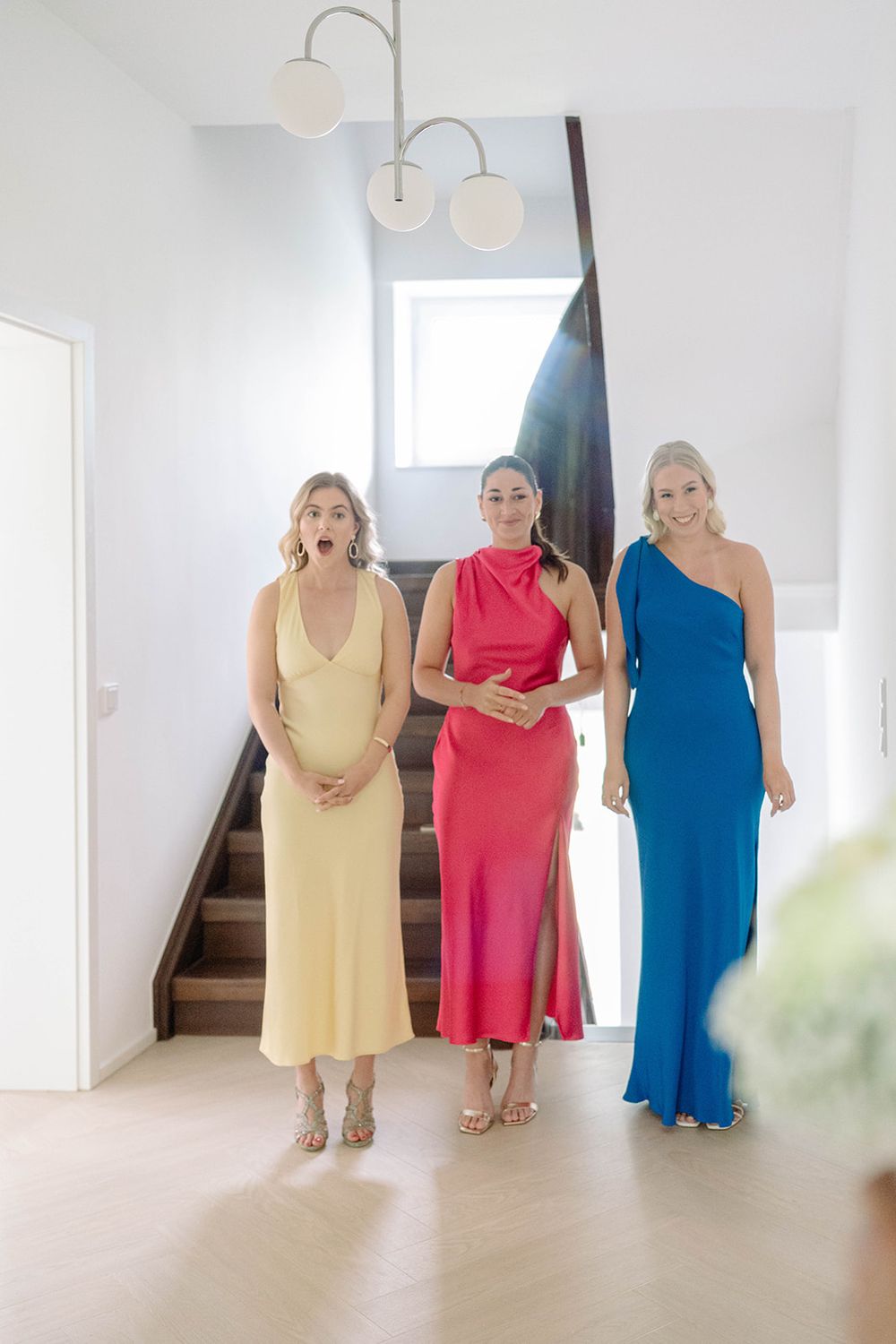 Women in colorful dresses standing together in a bright white interior space.
