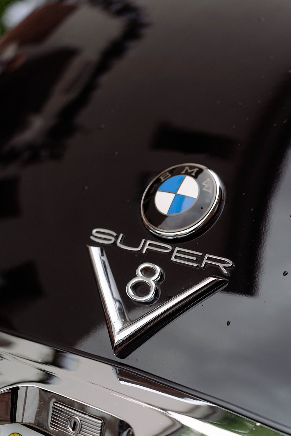 Close-up details of BMW Super V8 badges and emblems on a black vehicle.