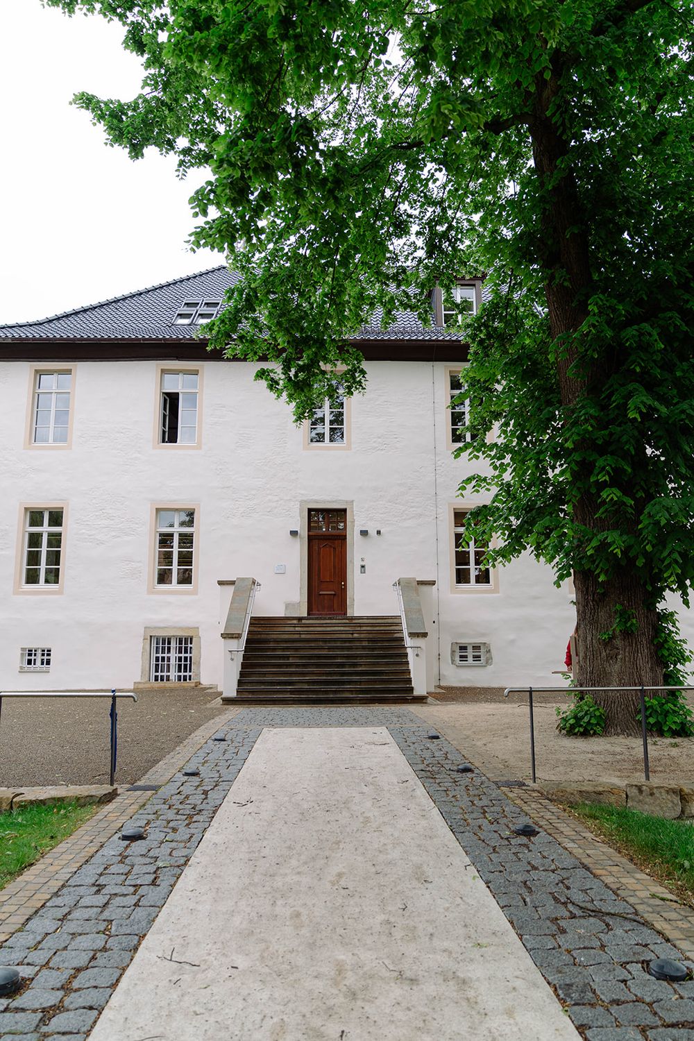 White stone building entrance with cobblestone path and green trees framing the scene.