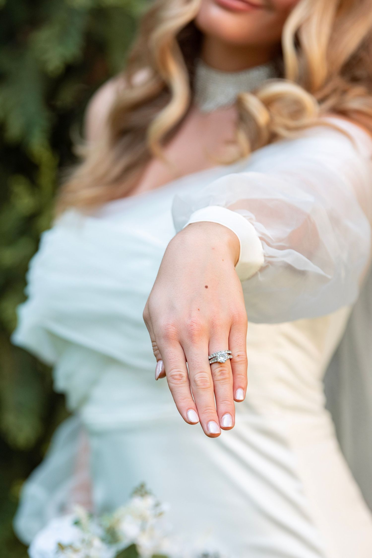 Close-up of bride's hand showing wedding rings with white dress detail.