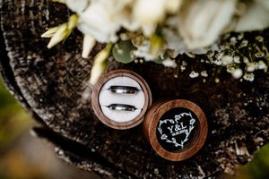 Two wedding rings displayed in wooden ring boxes with decorative details on a rustic wood surface.