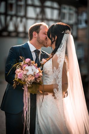 Romantic sunset wedding portrait with couple sharing tender moment and holding floral bouquet.