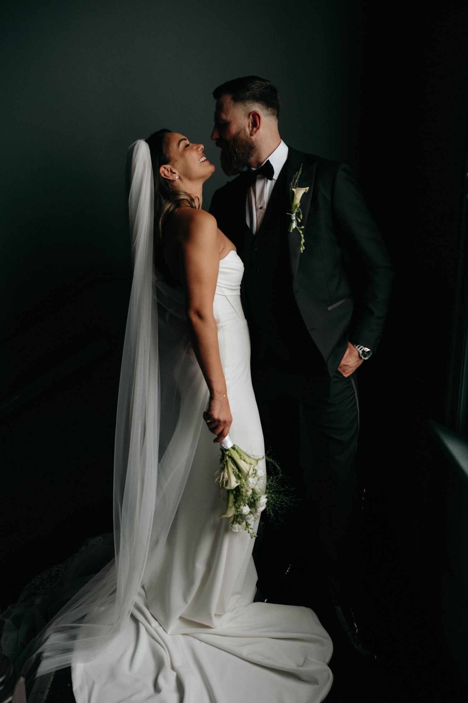 A bride and groom share an intimate moment in dramatic lighting against a dark background during their wedding portraits.