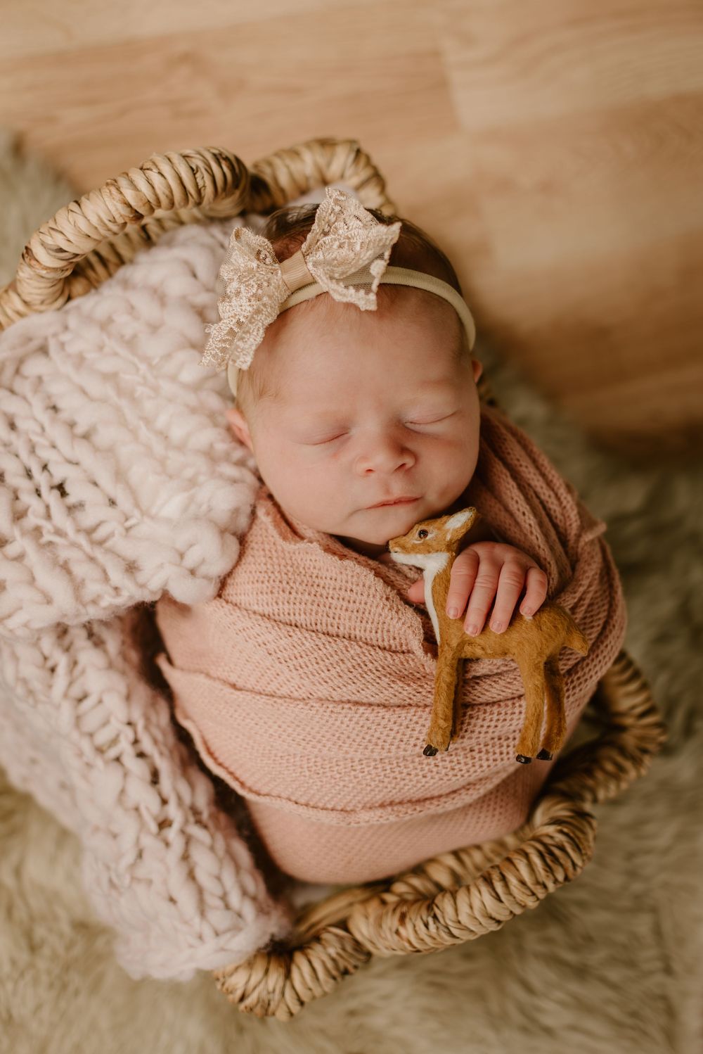 Sleeping newborn wrapped in pink knit fabric with lace blanket and delicate headband.