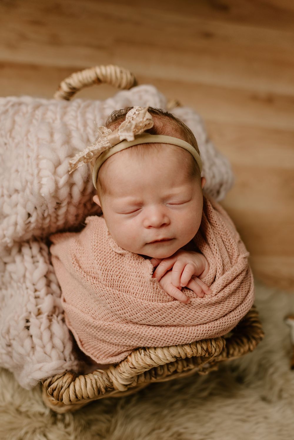 Peaceful newborn baby sleeping on textured blanket wearing soft pink wrap and headband.