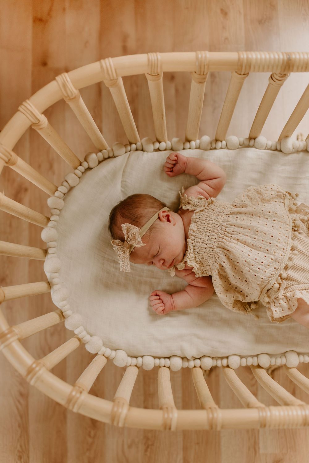 Newborn baby sleeping peacefully in vintage-style white bassinet wearing lace dress.
