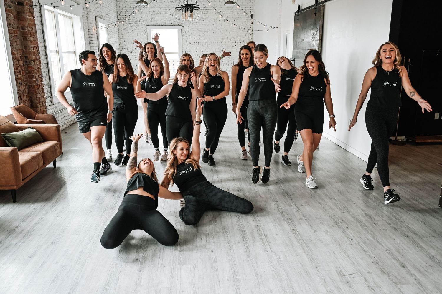 Group fitness class participants pose together in a bright white studio space.