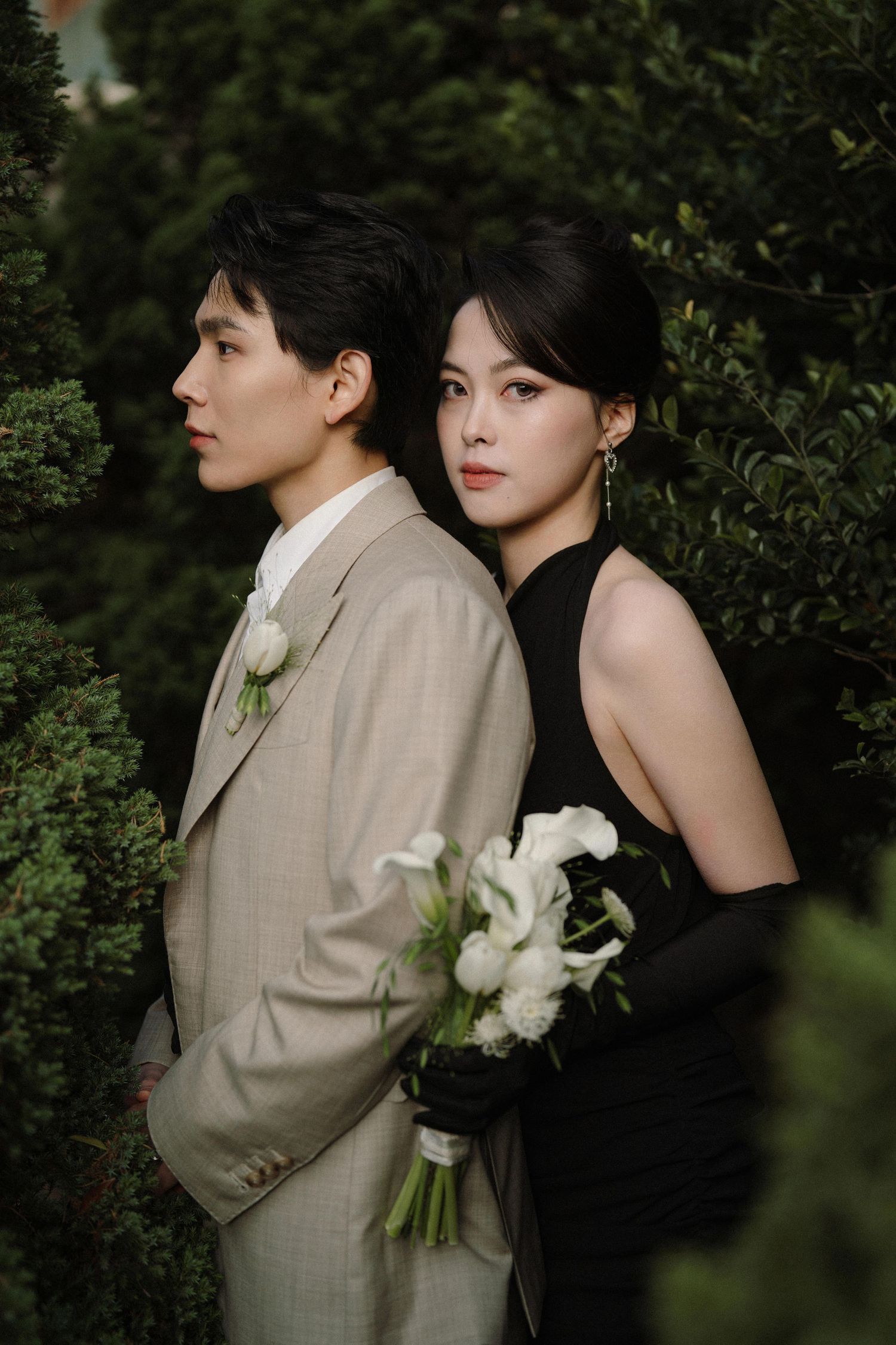 Artistic wedding photo showing a couple in beige suit and black dress holding white flowers.