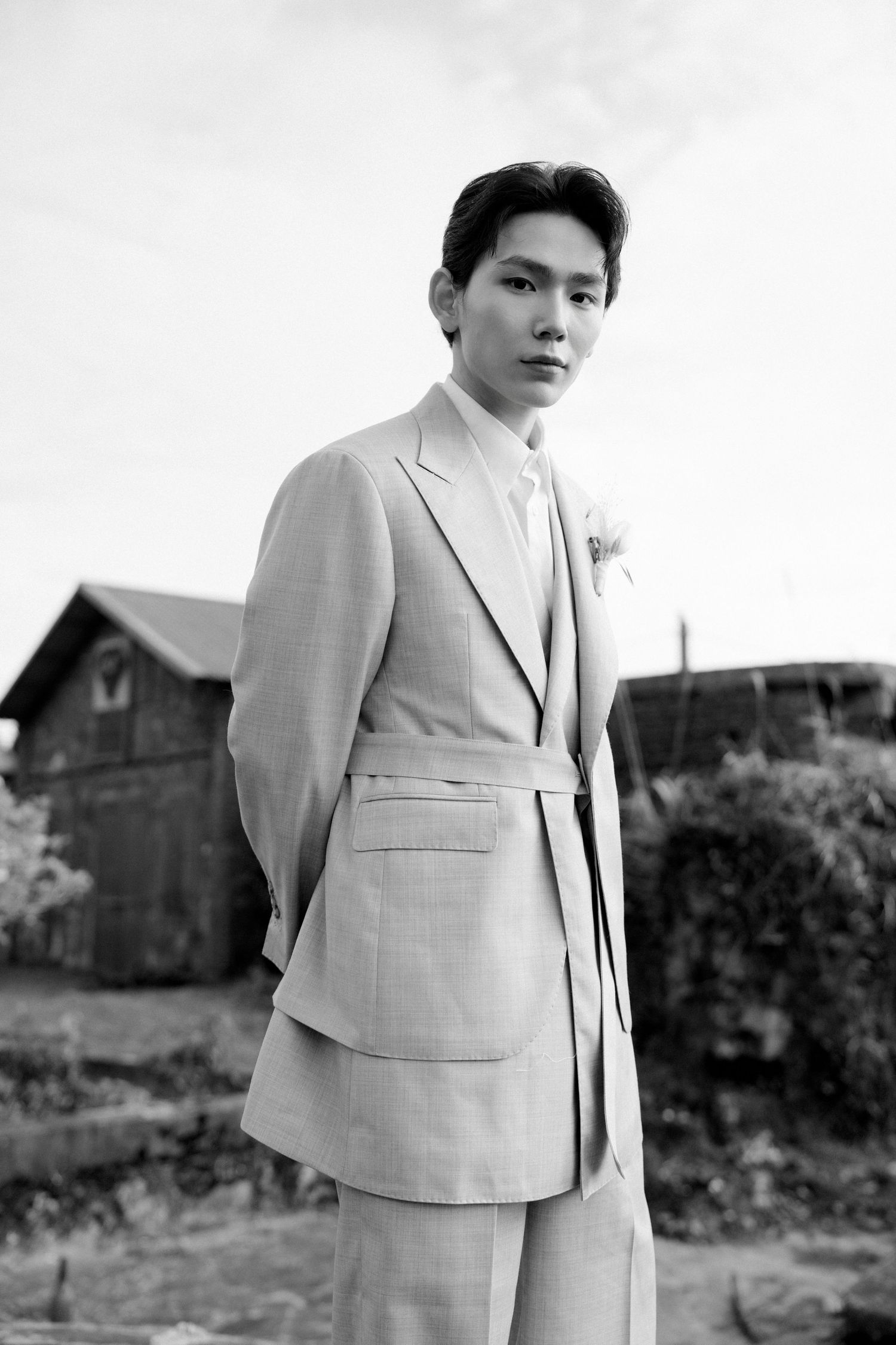 Elegant portrait in beige suit against a rustic countryside backdrop.