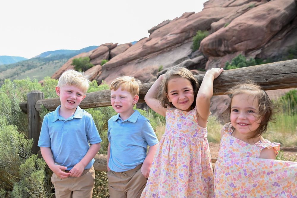 Four children posing together in front of red rocks at a scenic overlook on a sunny day.