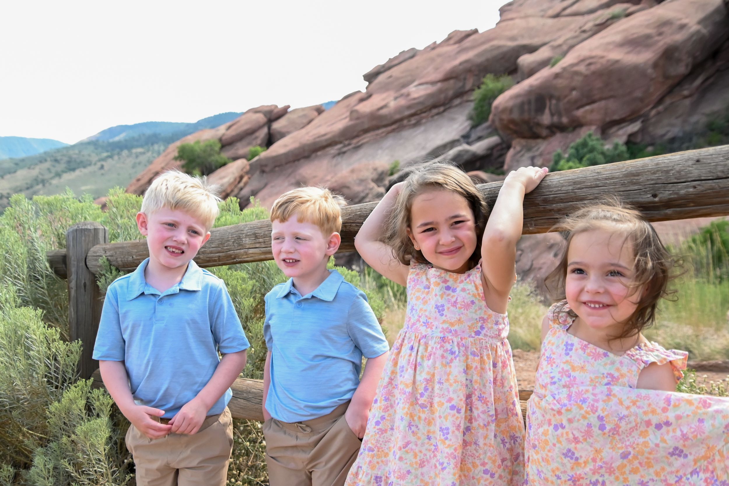 Four children posing together in front of red rocks at a scenic overlook on a sunny day.