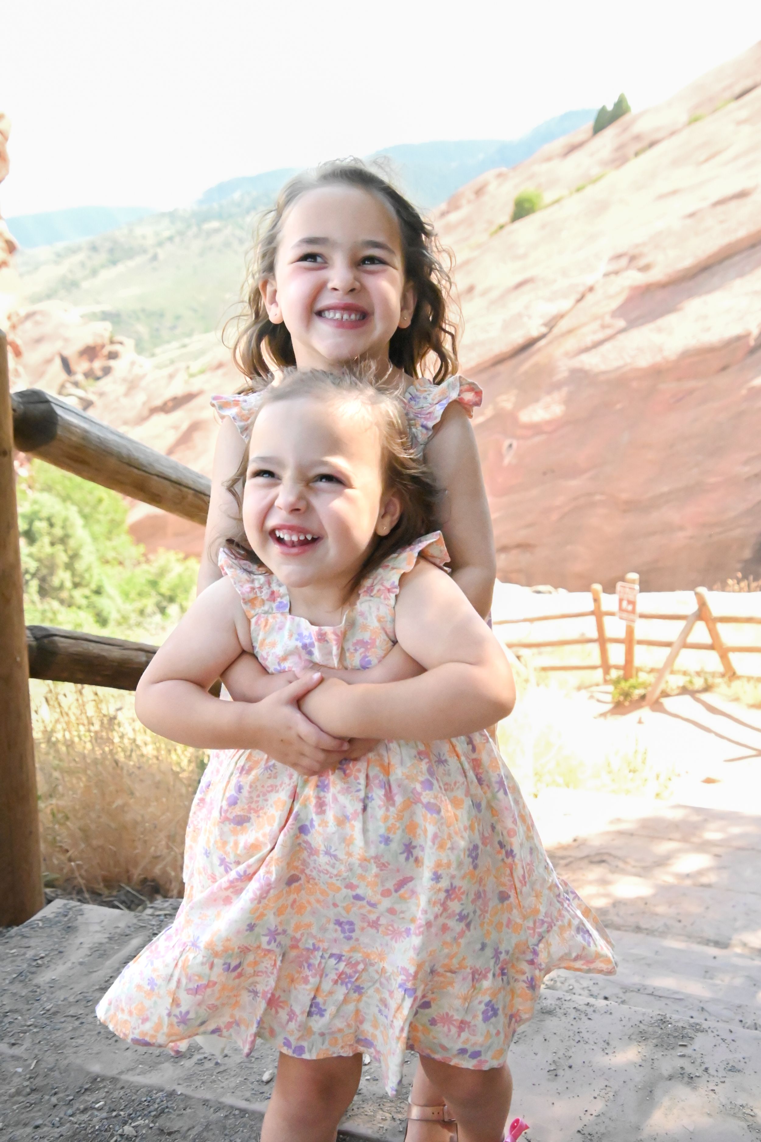 A joyful young child in a floral dress plays and poses outdoors against red rock formations at a scenic park.