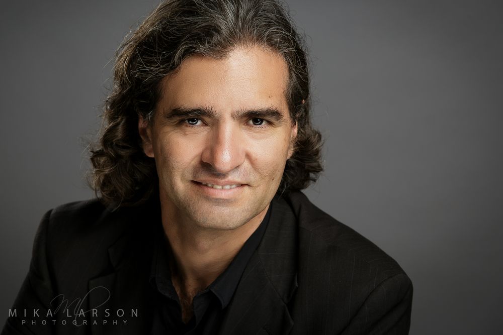 Professional studio headshot in black shirt against grey backdrop highlighting dramatic lighting and expression. Mika Larson Photography.