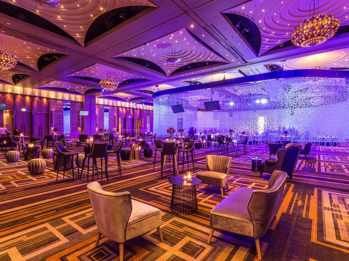 Elegant hotel ballroom with purple uplighting, geometric carpet patterns, and modern lounge seating creates a luxurious atmosphere.