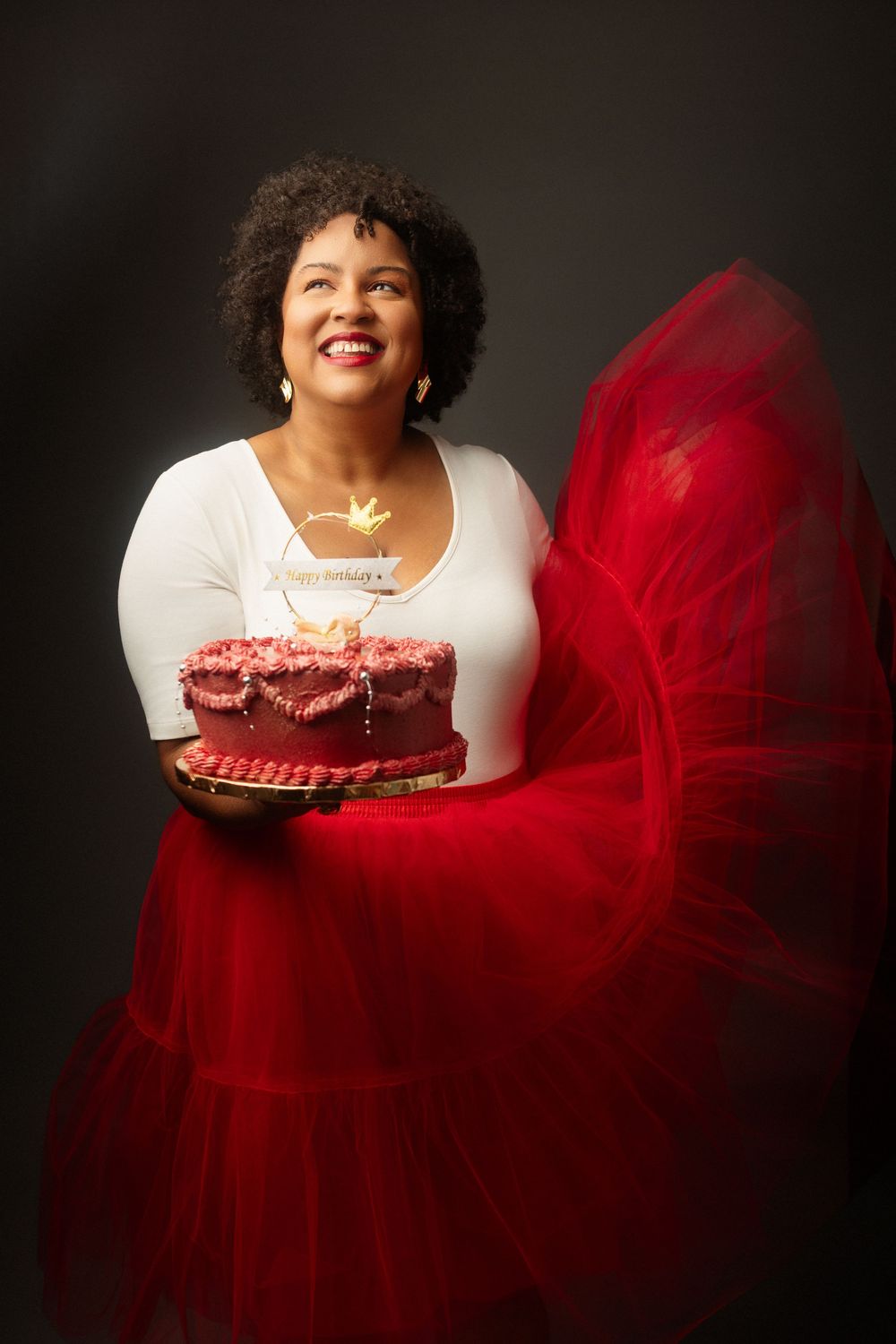 A stunning portrait series featuring a vibrant red tulle dress against a dark background in dramatic lighting.