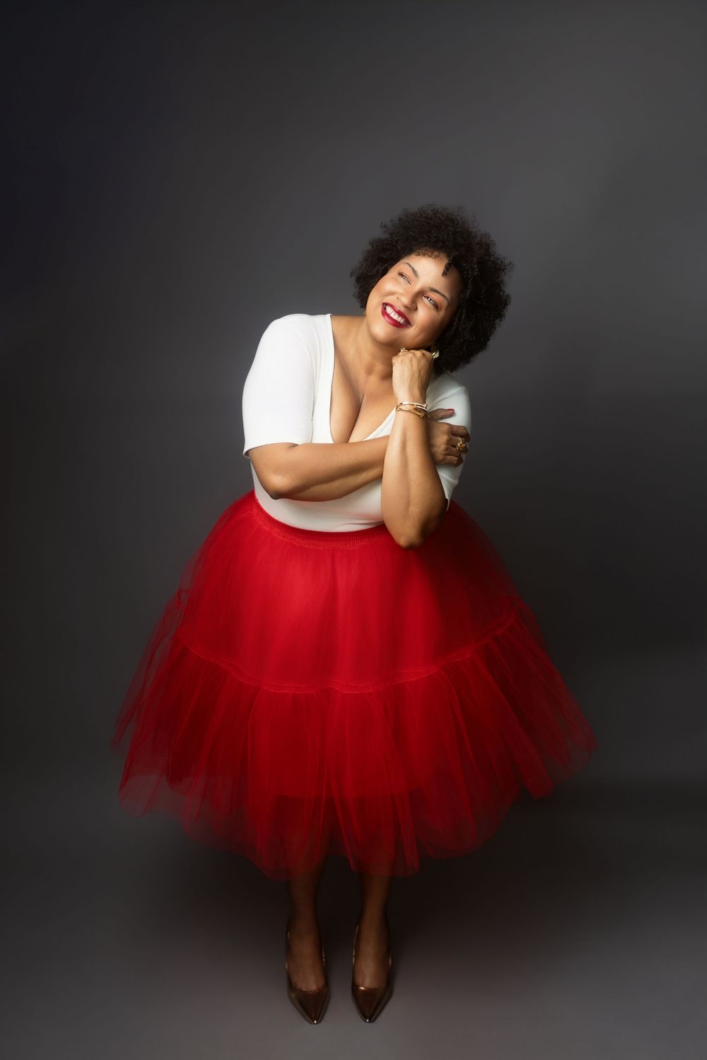 A figure in a white top and dramatic red tulle skirt strikes playful poses against a dark background in a photo series.
