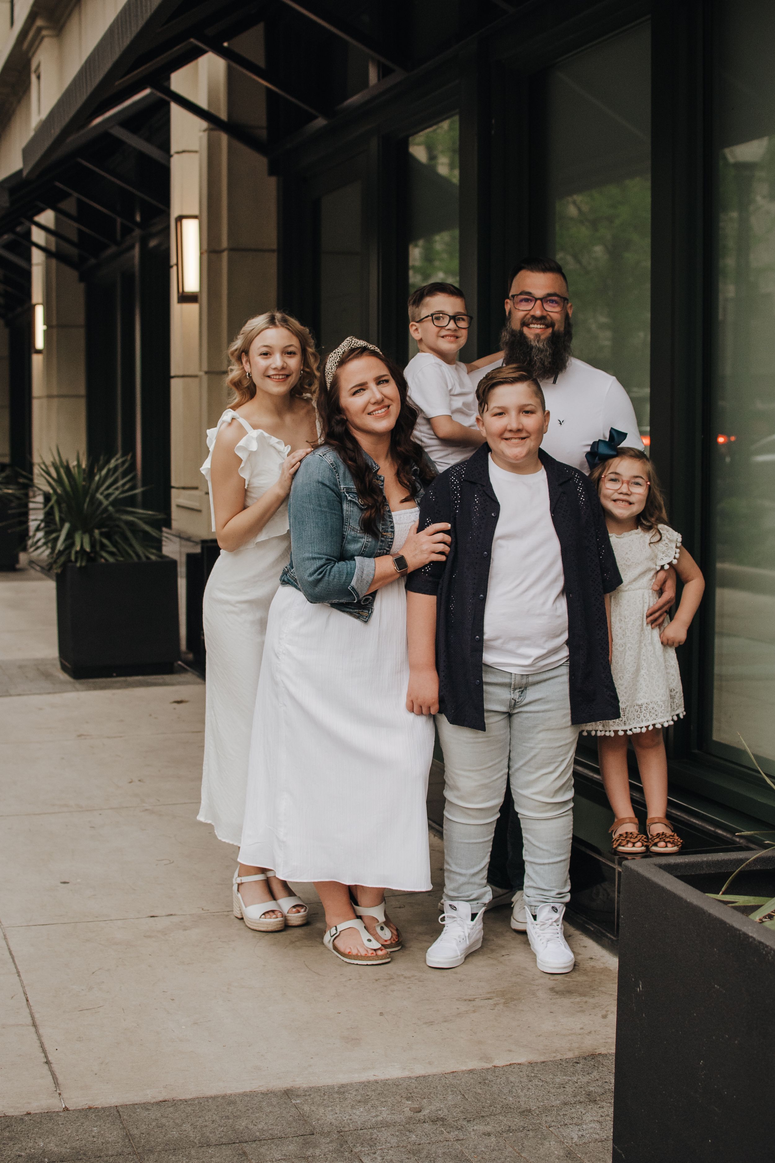 Extended family in coordinated white and black outfits poses casually together on a porch for outdoor photos.
