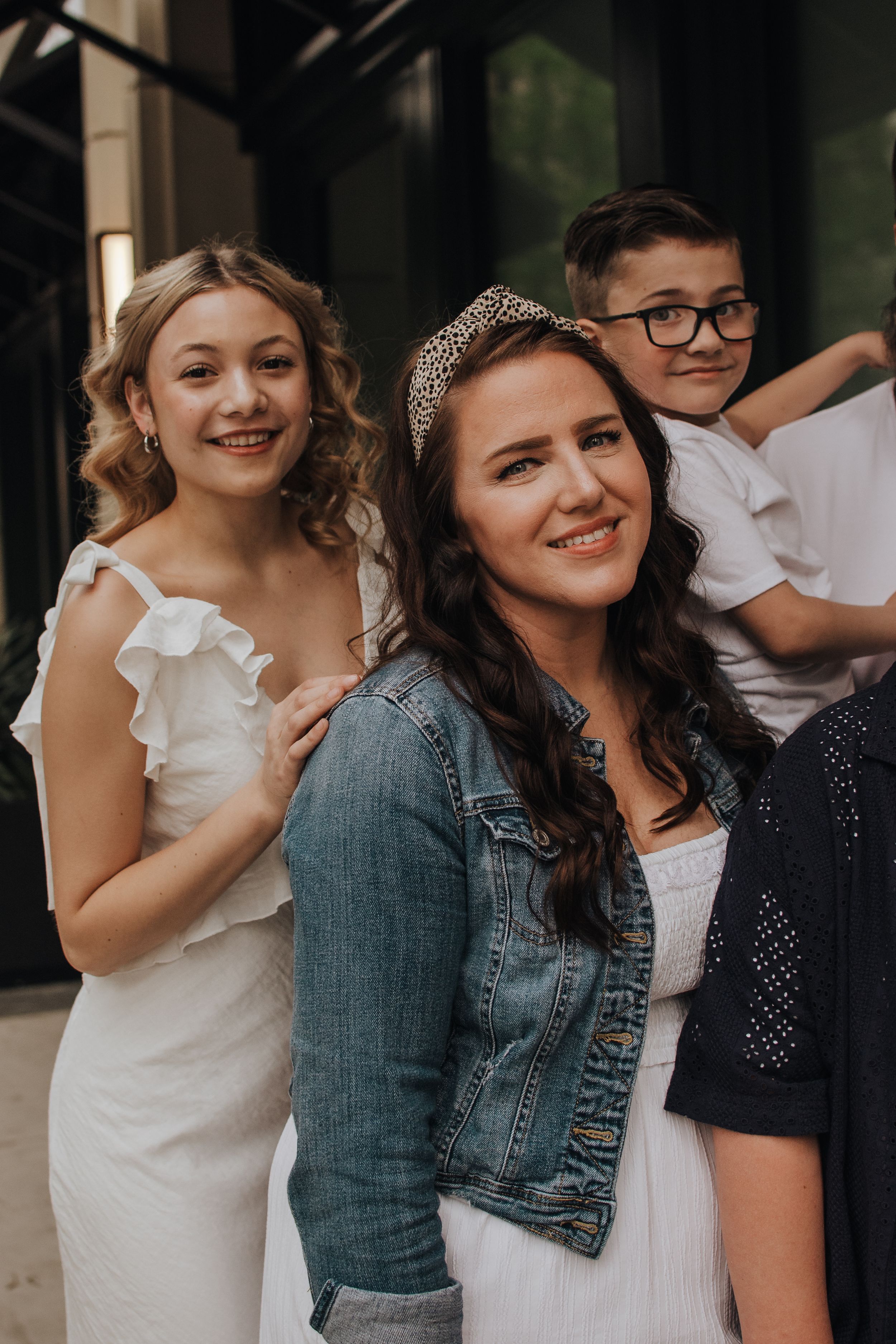 Group poses together wearing mix of denim, white, and dark clothing at casual outdoor event.