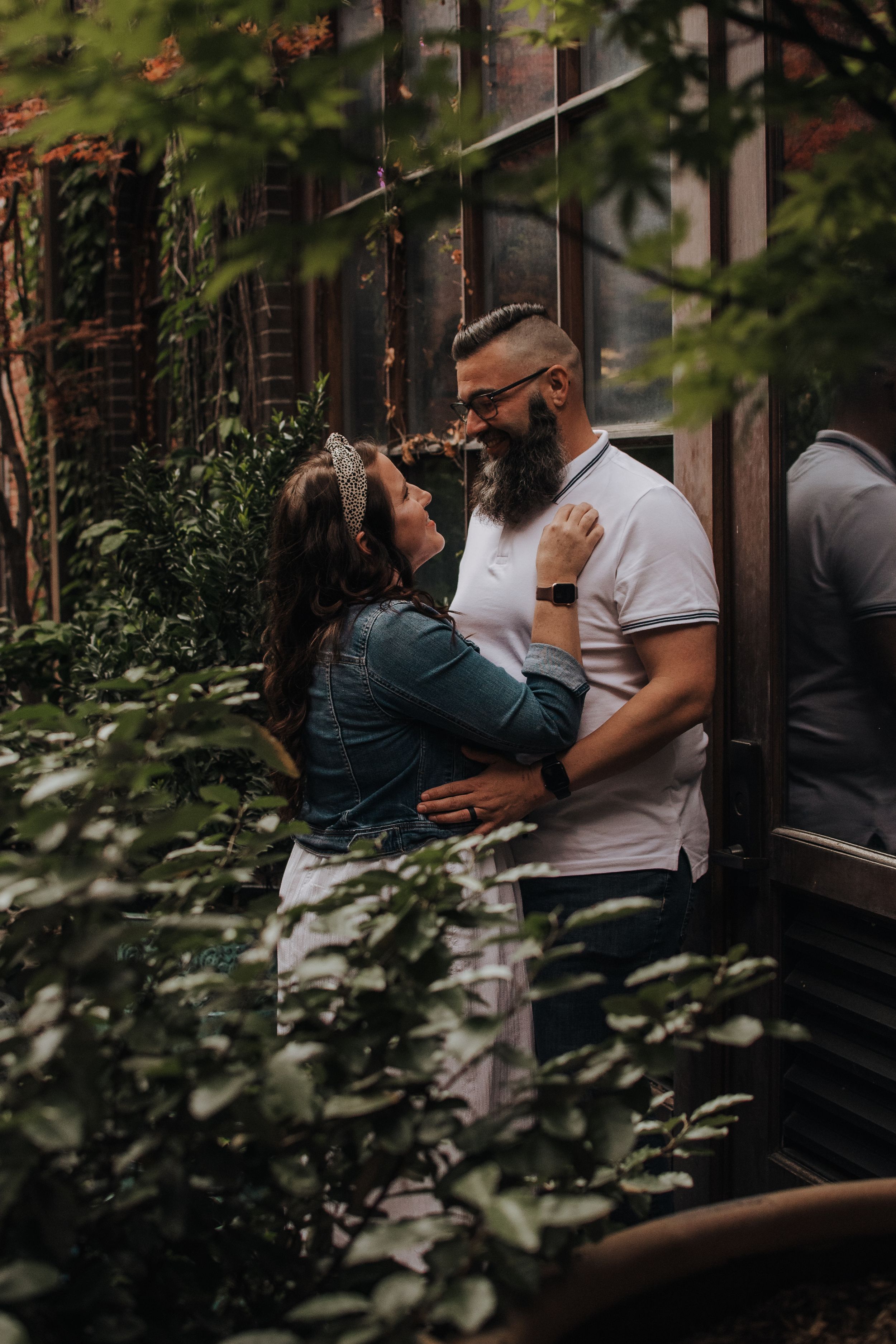 Two people share an intimate moment in a garden setting with green foliage in the background.