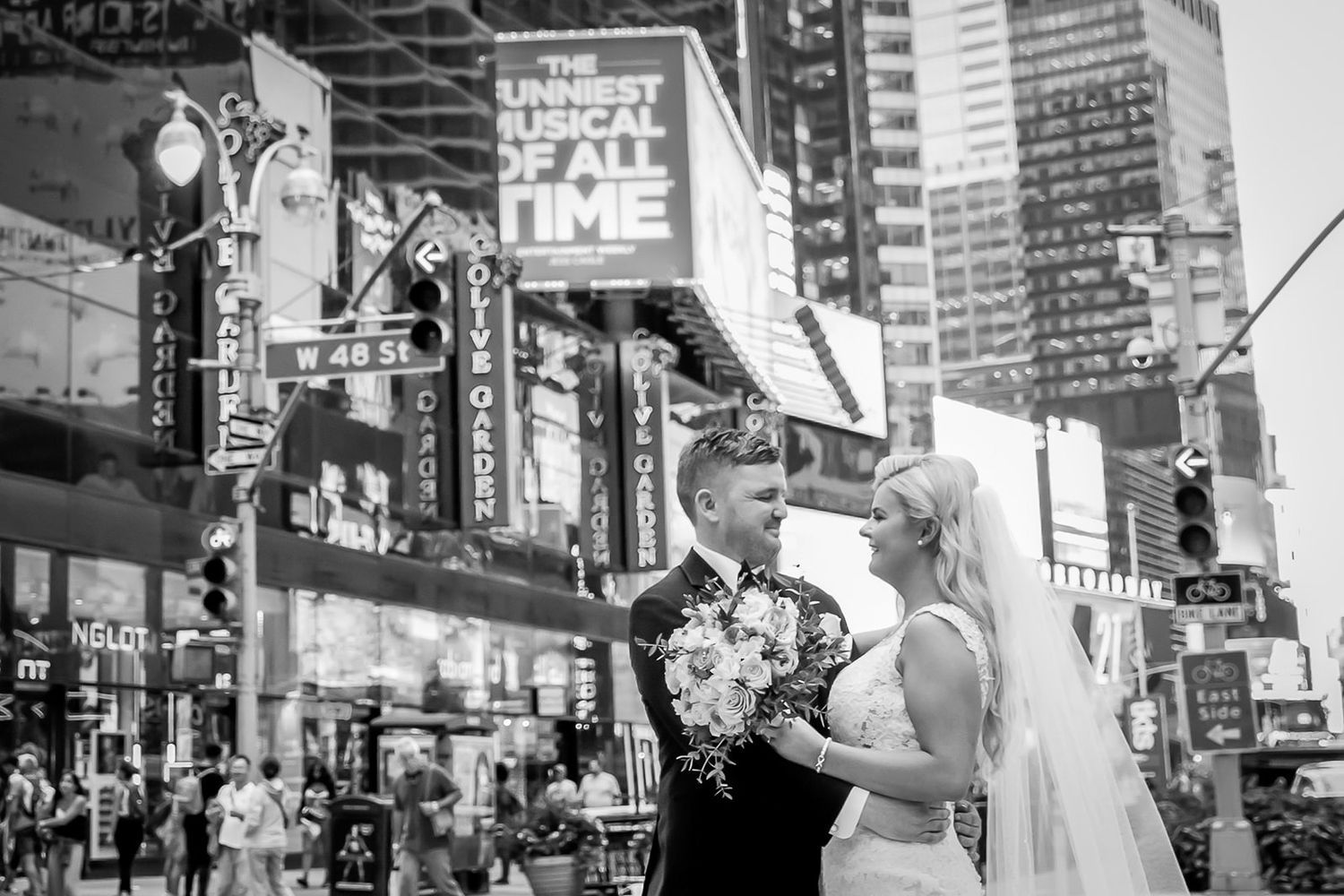 Diverse crowd gathers near digital billboards and signage in Times Square in New York City at night.