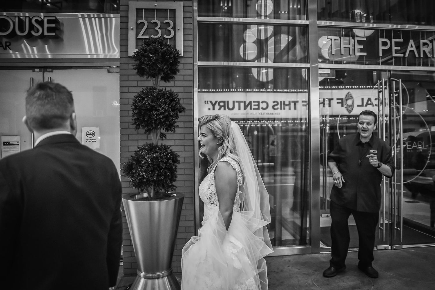 Black and white urban wedding scene with the couple walking past buildings and potted trees in New York City.
