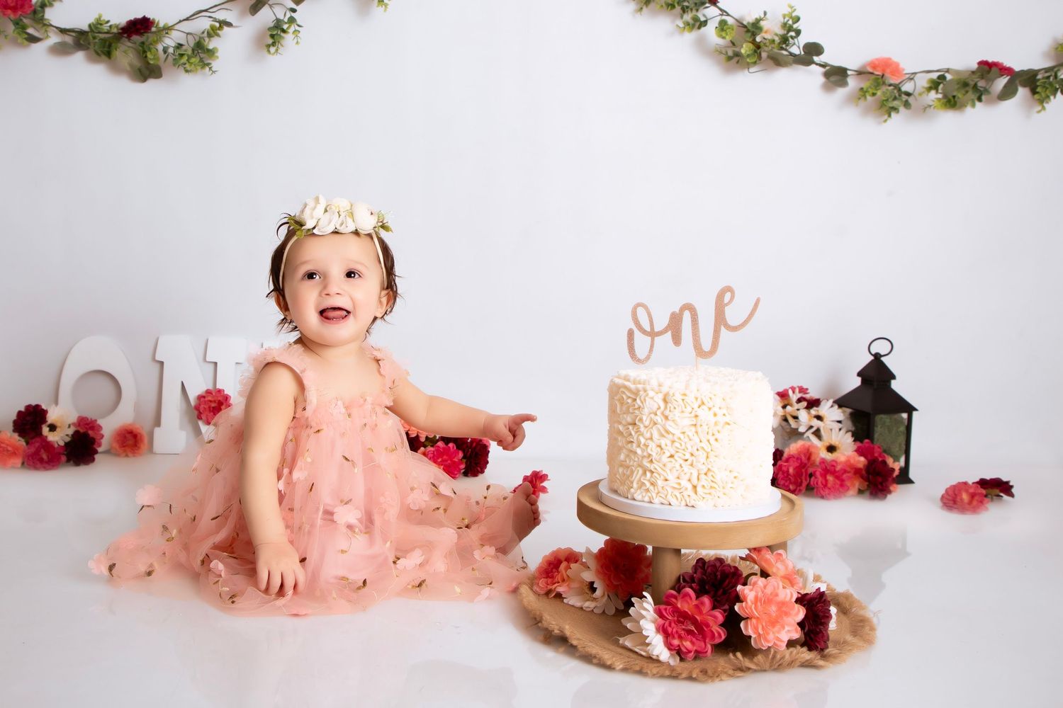 Themed photography setup with pink flowers and delicate decor in white for cake smash celebration session.