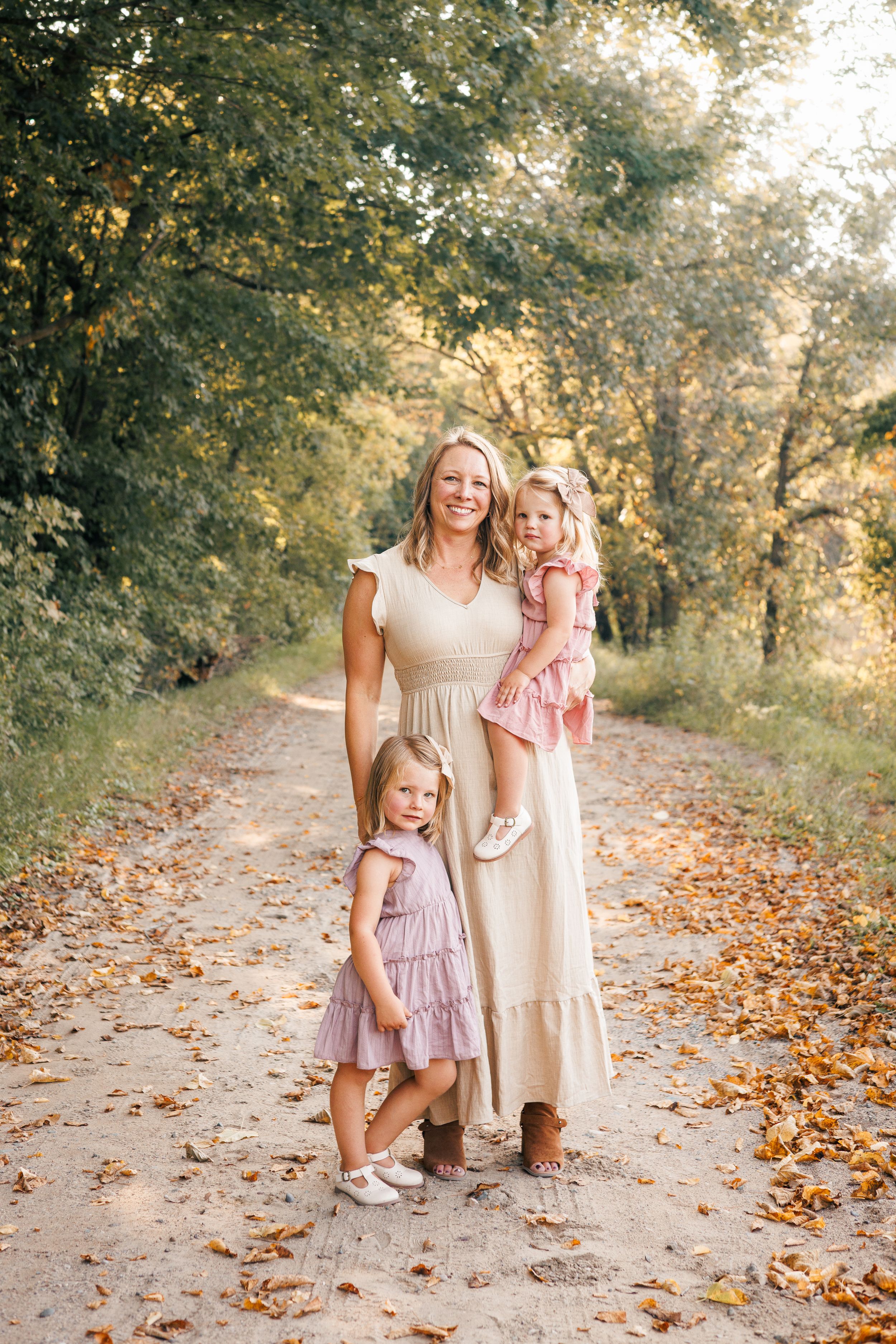 A family stands together on a leaf-covered forest path during golden hour in autumn.