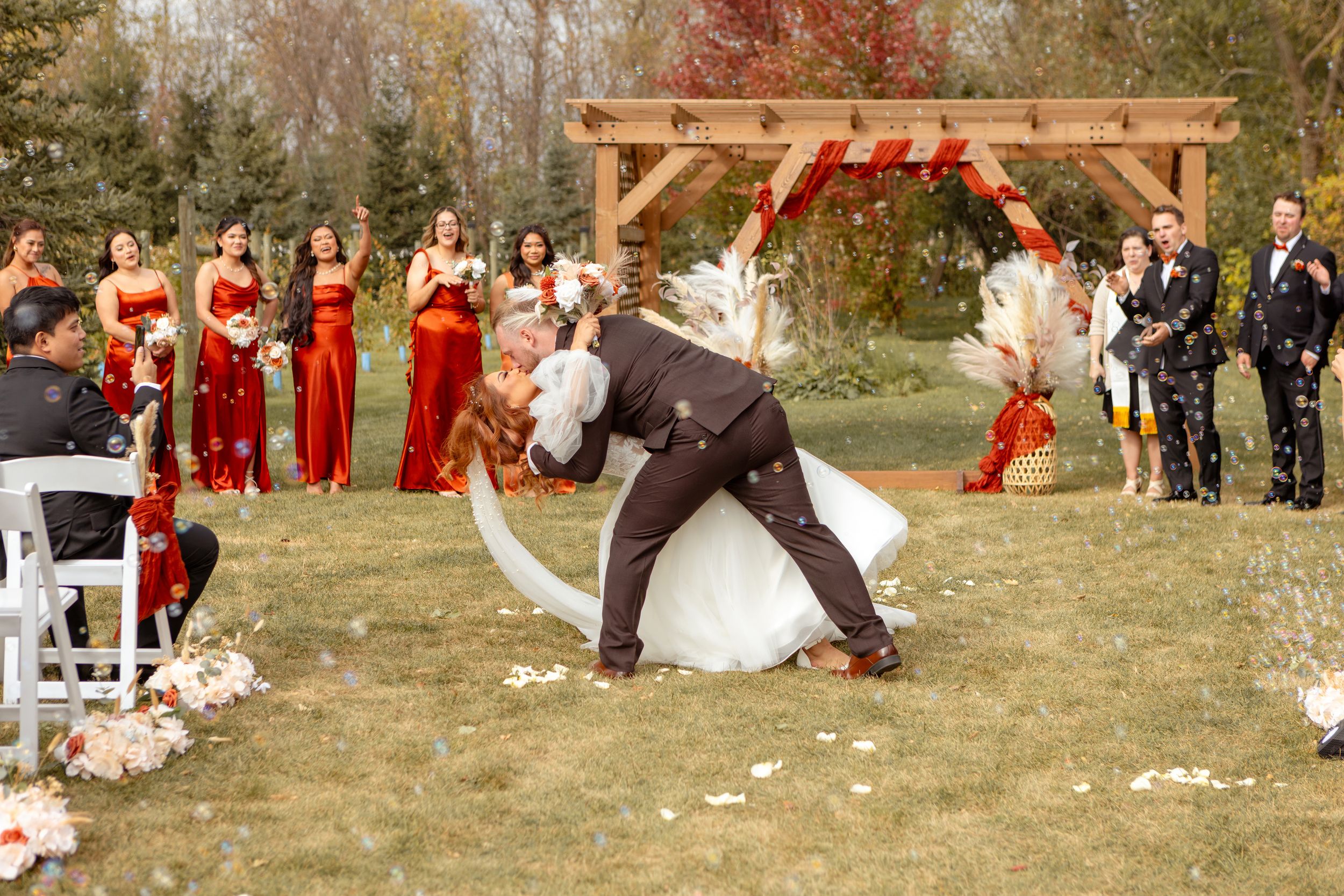 Wedding guests watch in amusement as a wooden arch structure falls during an outdoor ceremony.