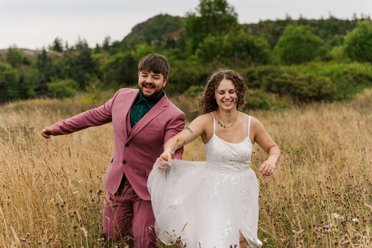 A couple strolls through a golden meadow during an outdoor photo session in a natural setting.