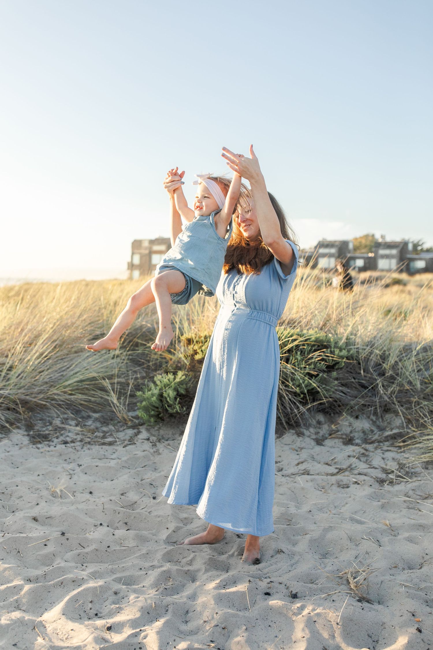 Woman in light blue dress dances gracefully on a sandy beach at sunset.