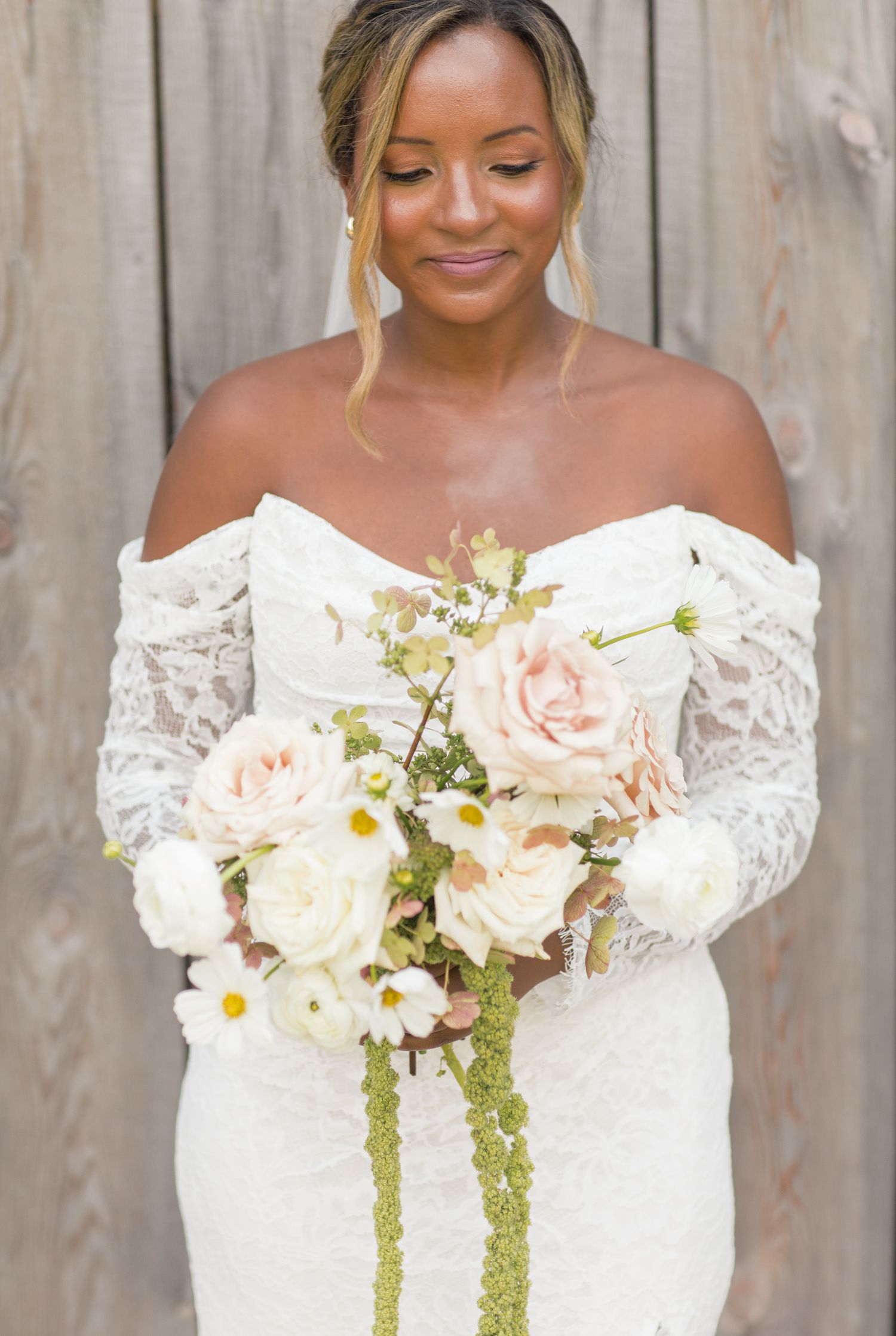 Beautiful bridal bouquet featuring blush pink and white roses with cascading greenery against an off-white lace gown.