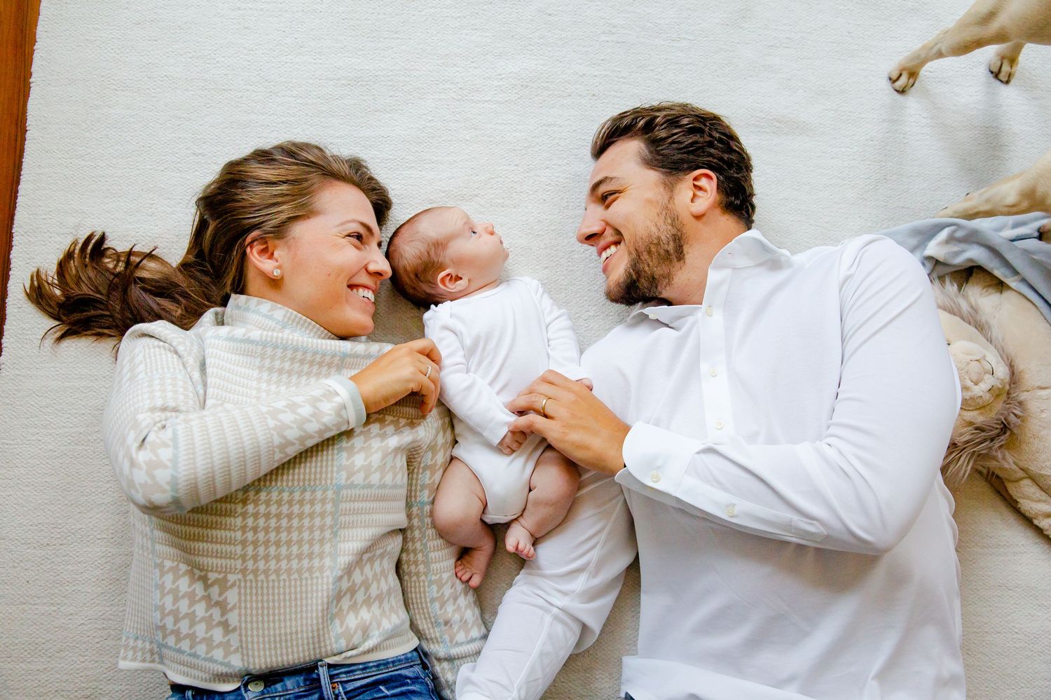Intimate, fun family photography in NYC. A happy family lying together on white blankets, sharing joyful moments with their young baby.