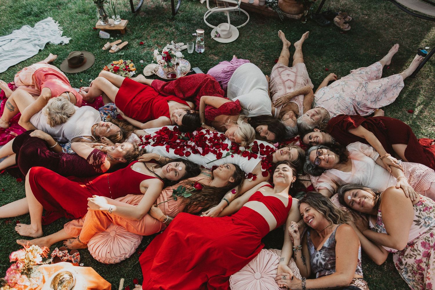 People lay on grass in red and pink dresses during an outdoor summer gathering.