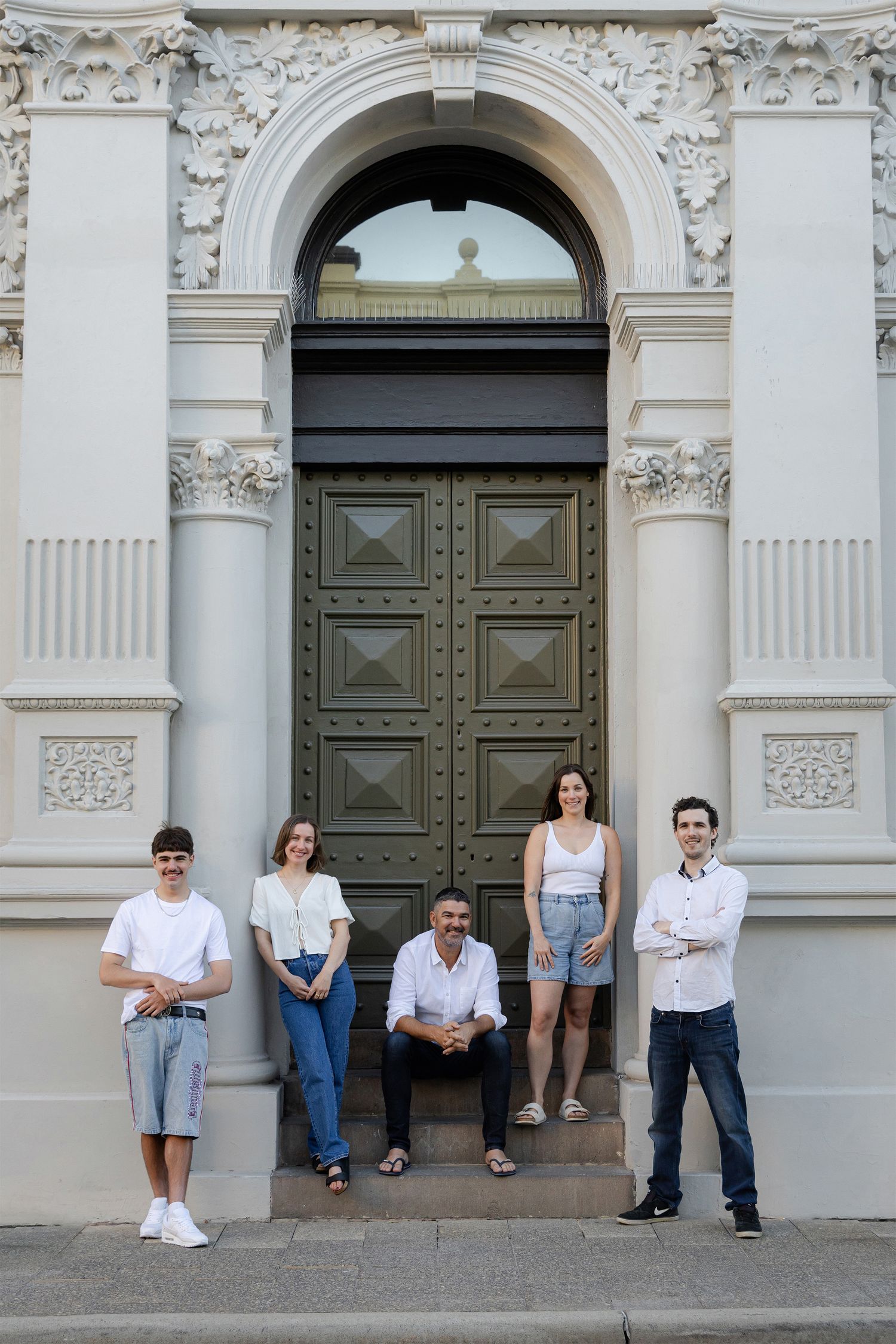 A group of people sitting together on stone steps outside against a beige textured wall.