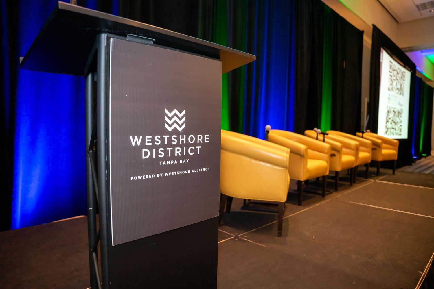 Corporate event stage area with professional lighting and branded displays in blue tones.