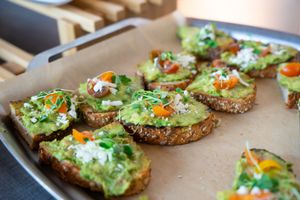 Appetizer platter featuring avocado toast bites garnished with fresh herbs and vegetables.