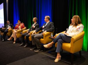 Panel discussion featuring speakers seated in yellow armchairs on stage with blue and green lighting effects.