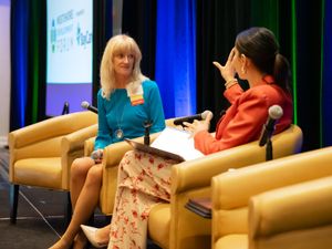 Two speakers engaged in conversation while seated in comfortable yellow armchairs on stage.