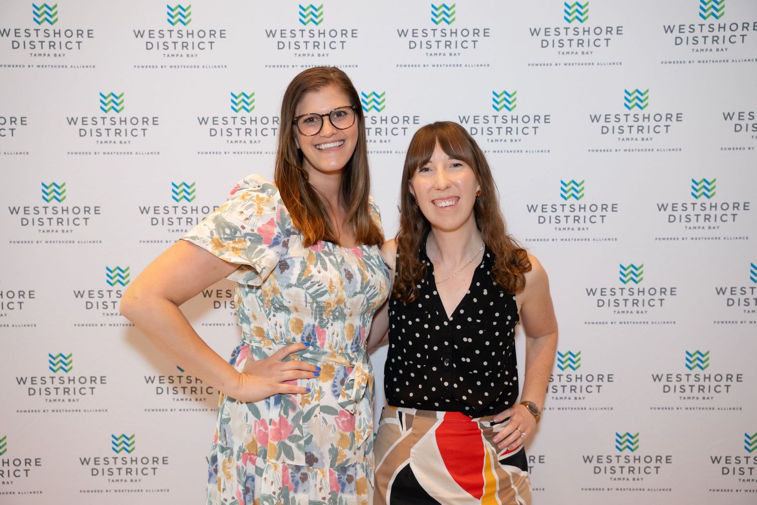 Two attendees posing in front of step-and-repeat banner at professional event.