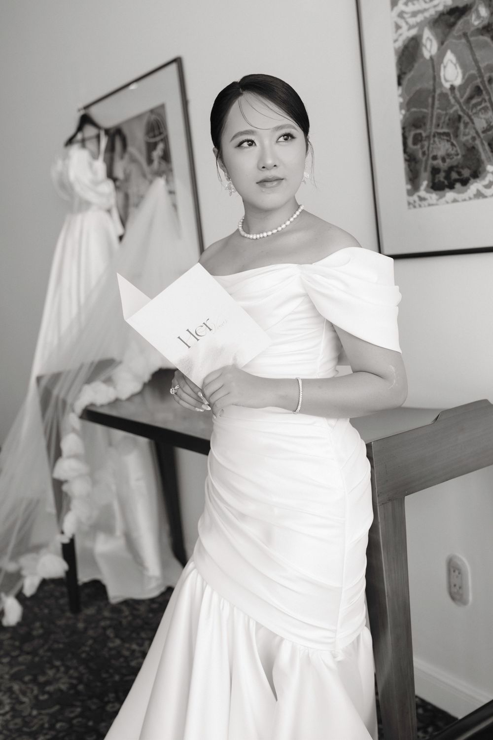 Elegant bride in off-shoulder mermaid wedding gown reading vows letter in black and white.