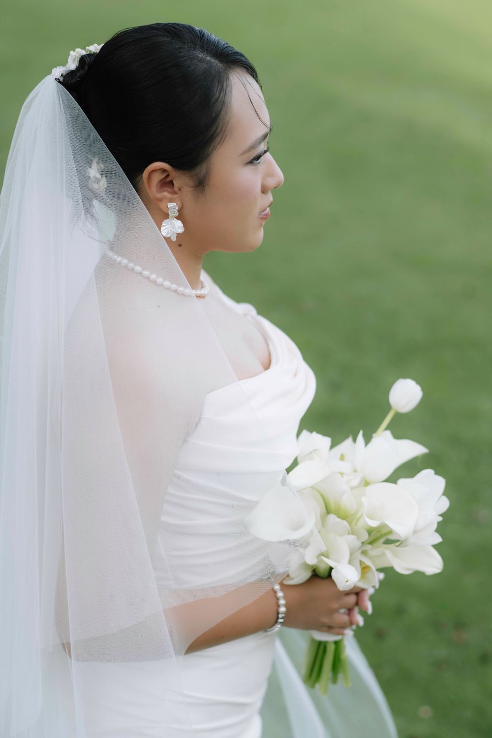 Side profile of Asian bride in white wedding dress and veil holding white calla lily bouquet.