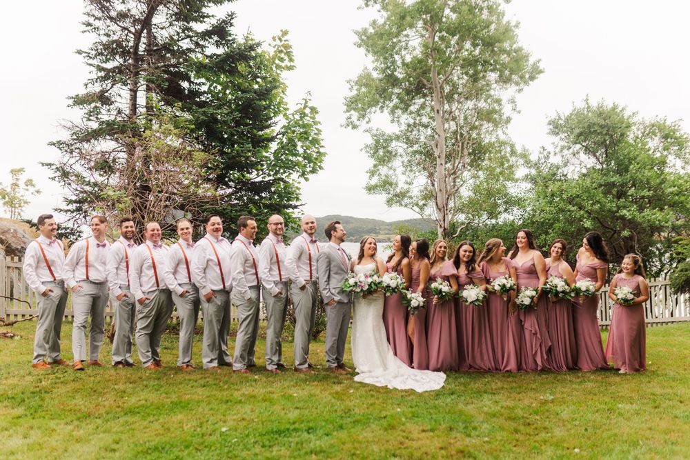 Bridal party lines up outdoors with groomsmen in gray suits and bridesmaids in dusty rose dresses.
