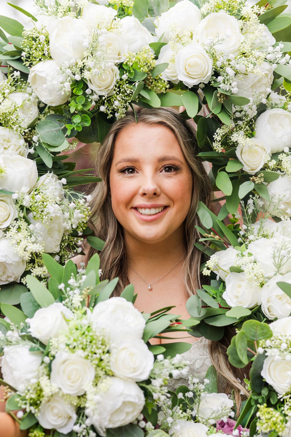 Bridal portrait surrounded by an elegant archway of white roses, hydrangeas, and fresh greenery.