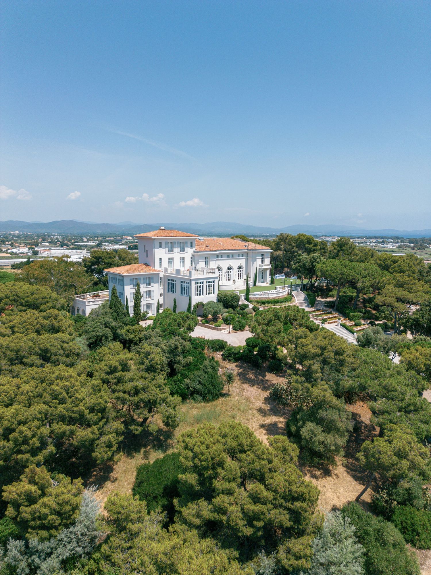 Panoramic coastal view of white Mediterranean villa Castel Bay, Hyères nestled among lush green trees with ocean vistas in the background.